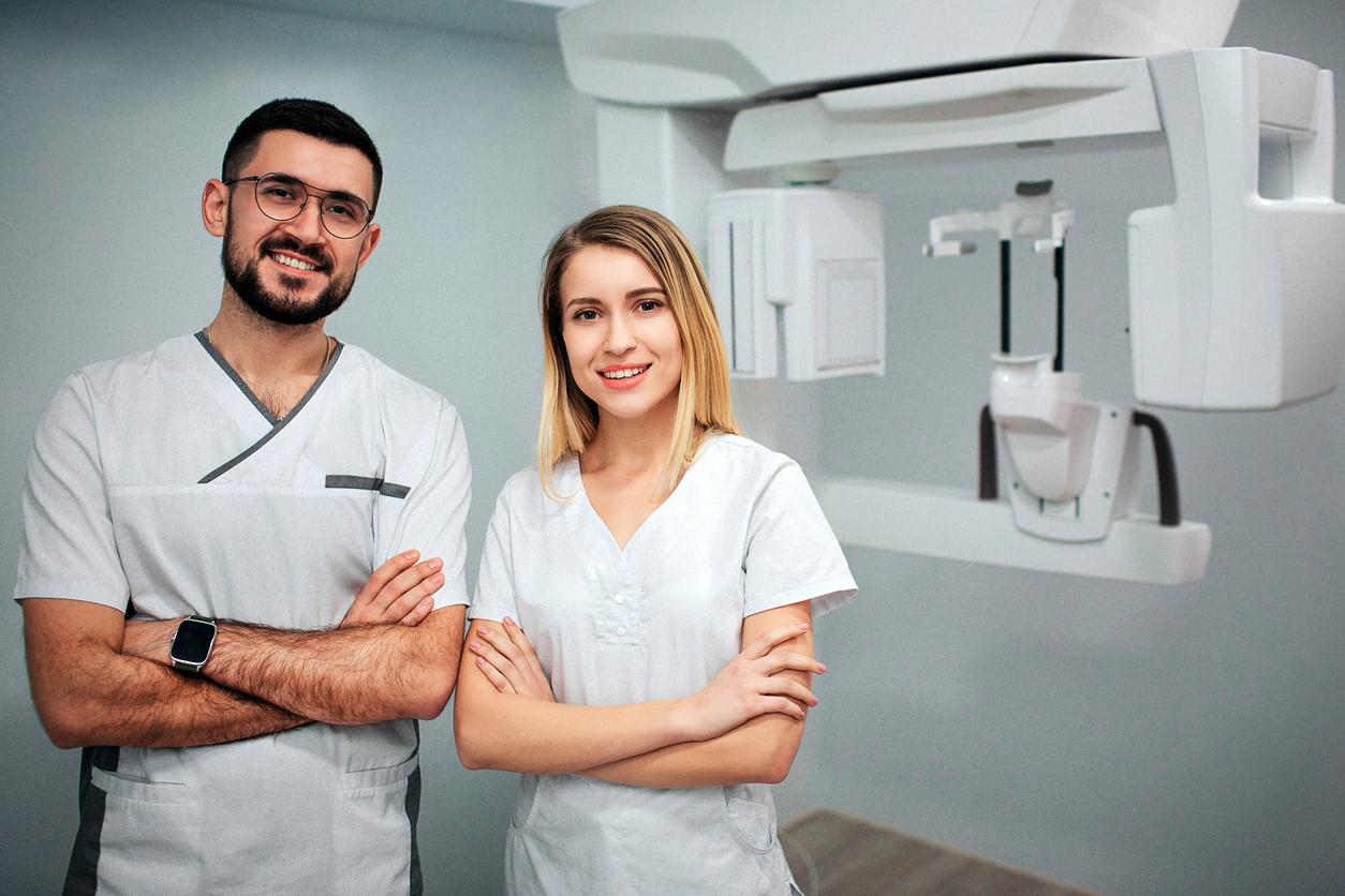 Two dentists stand in x-ray room and pose to camera. They smile and hold hands cossed. Professionals on picture