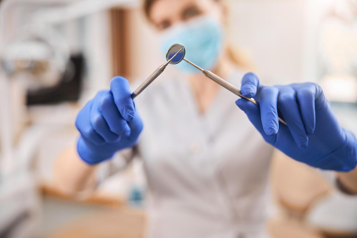 Close-up photo of a dental extractor and mouth mirror being held criss-crossed by a dental technician