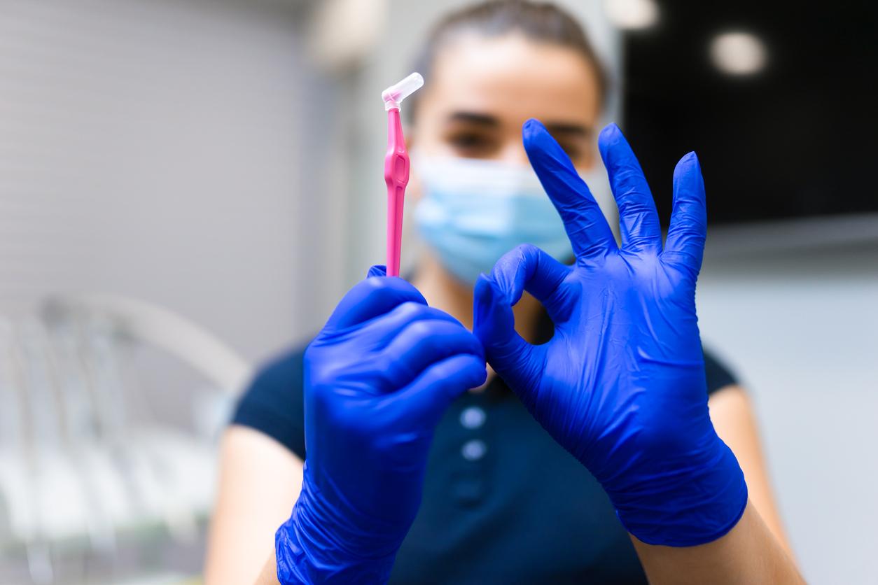 Dentist holds brush for cleaning the interdental spaces and shows ok gesture